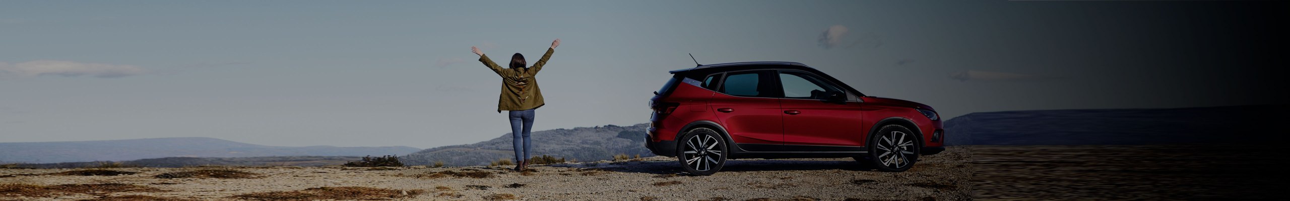 Woman on hill of the mountain next to a SEAT Arona in red colour