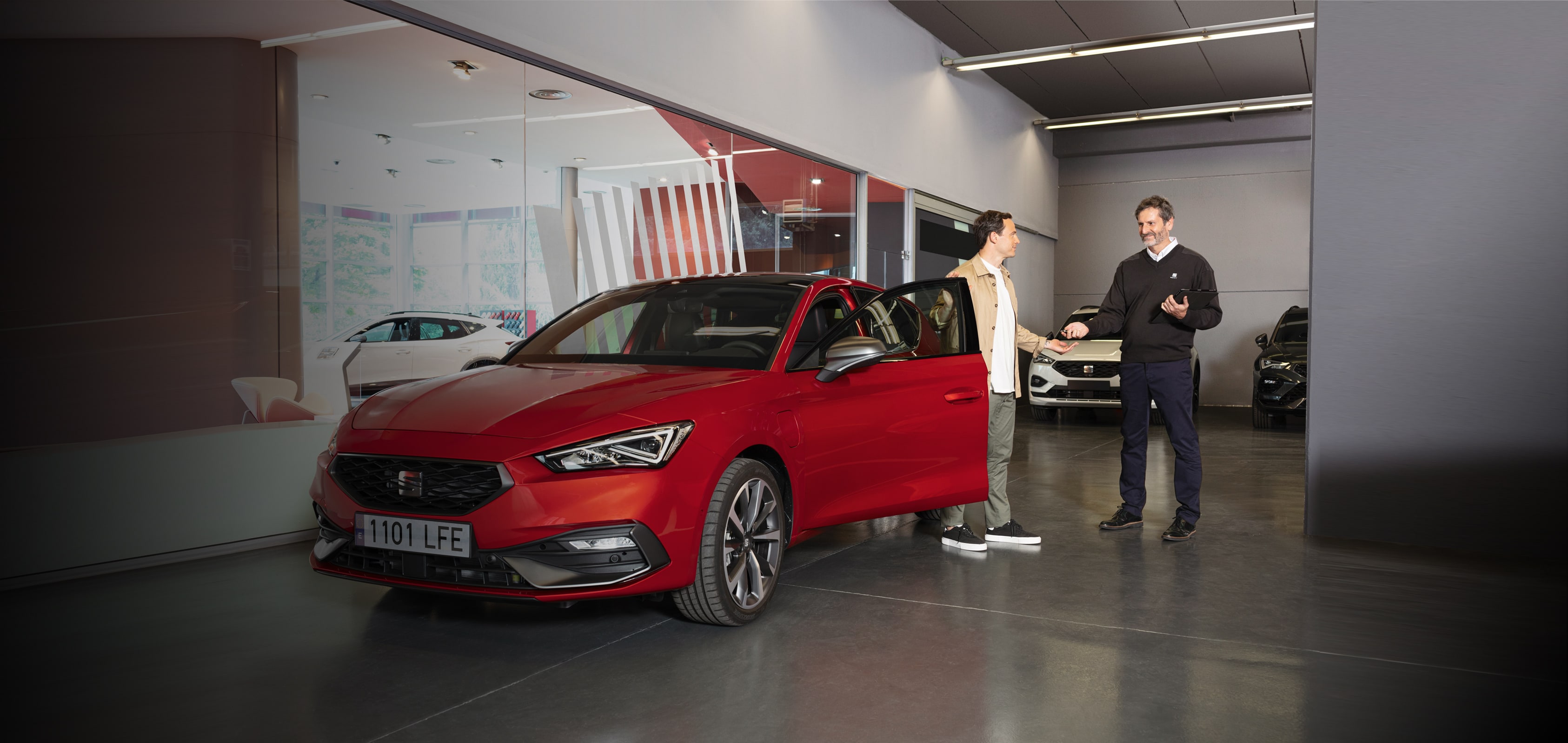 Two men standing beside a red SEAT car with the driver’s door open