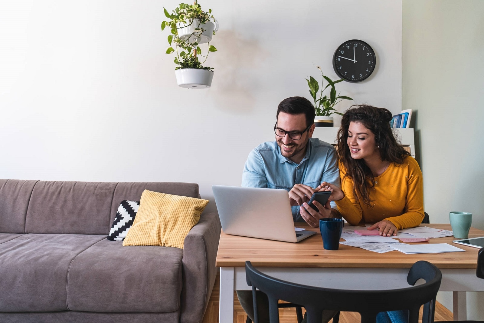 A couple sitting at a table, smiling as they view the SEAT Financial Services customer portal on their laptop.