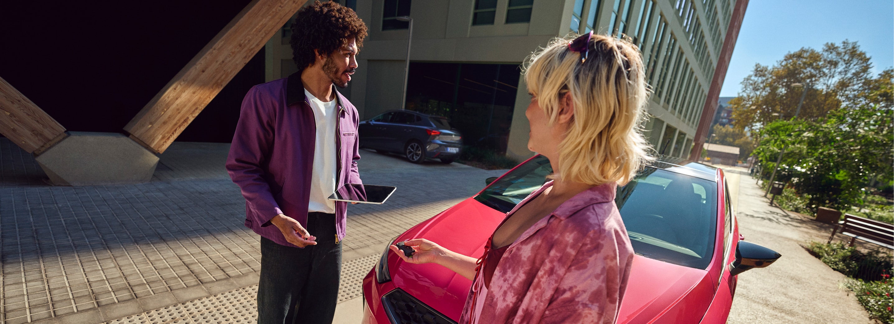 Two people standing next to a red SEAT Ibiza in an urban setting, holding car keys and a tablet.  
