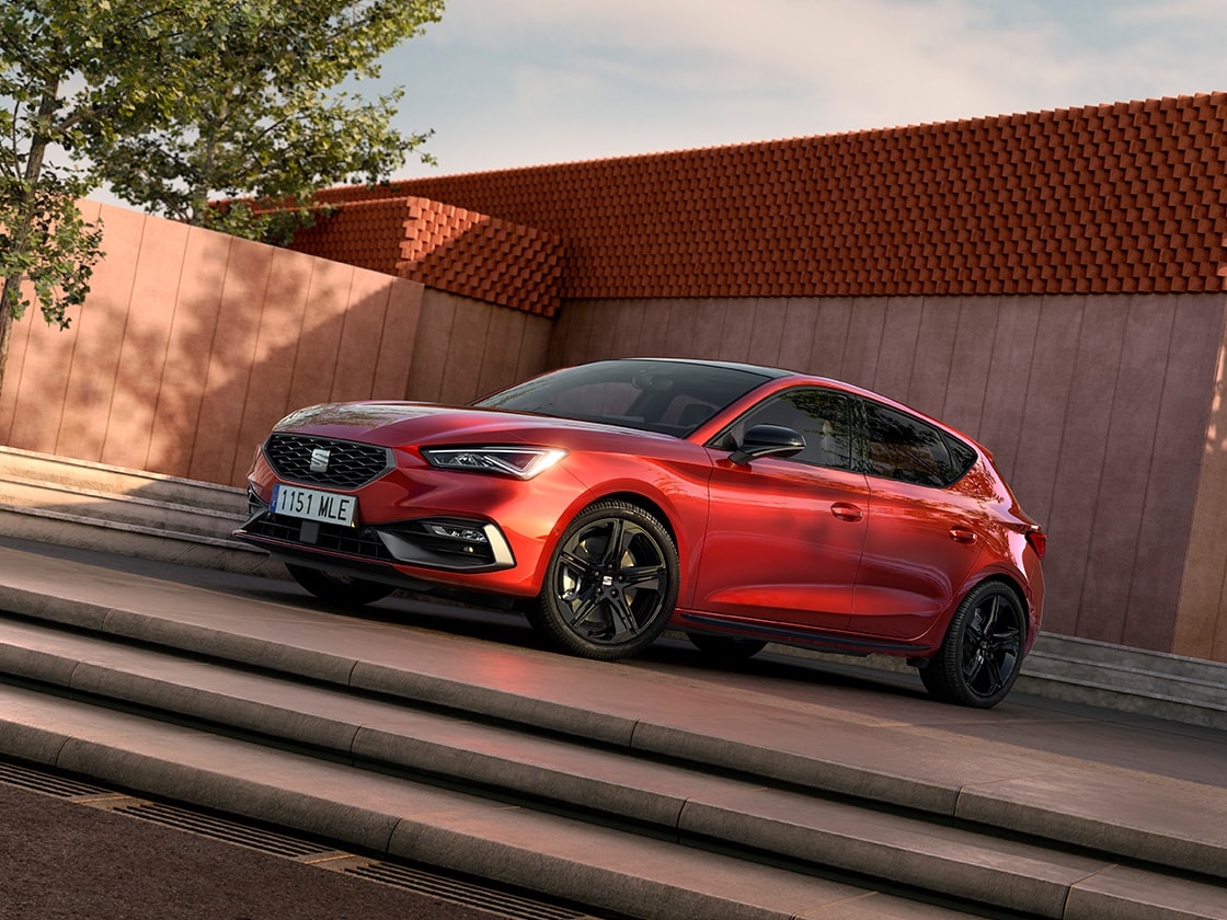 Side view of the SEAT Leon NF 5D in desire in a sunny spot with a building and stairs behind.