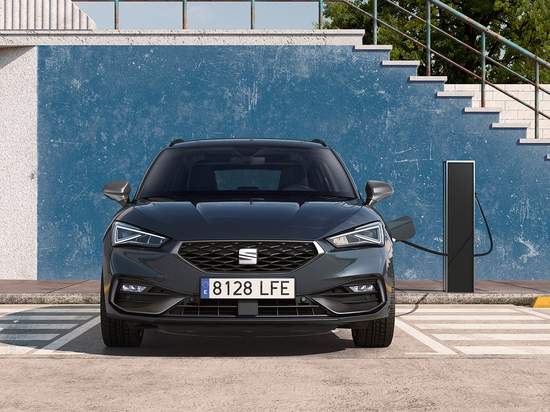 The seat leon sportstourer e hybrid, a hybrid electric car, parked in a parking spot next to a charging station outdoors, showcasing the e manager feature for impressive value.