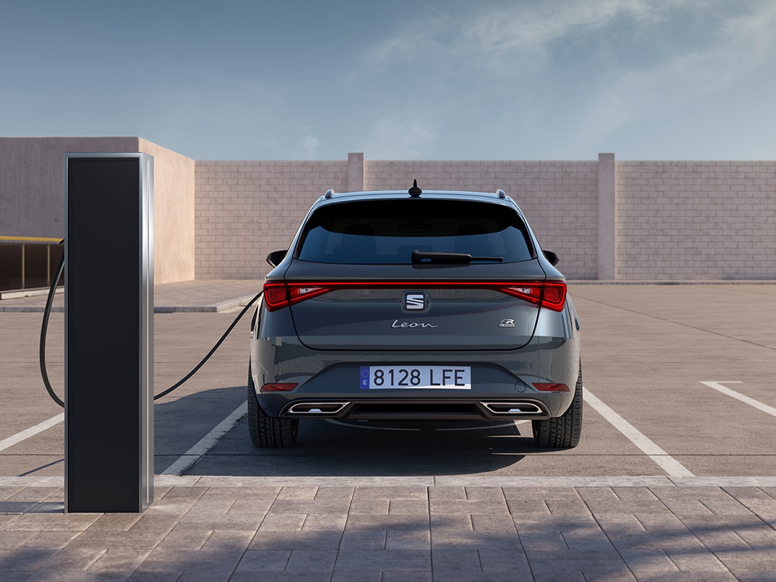 Rear view of the seat leon sportstourer fr automatic car charging at a station, a new hatchback for 2025 in magnetic grey, complete with rear parking sensors and led headlights and taillights.