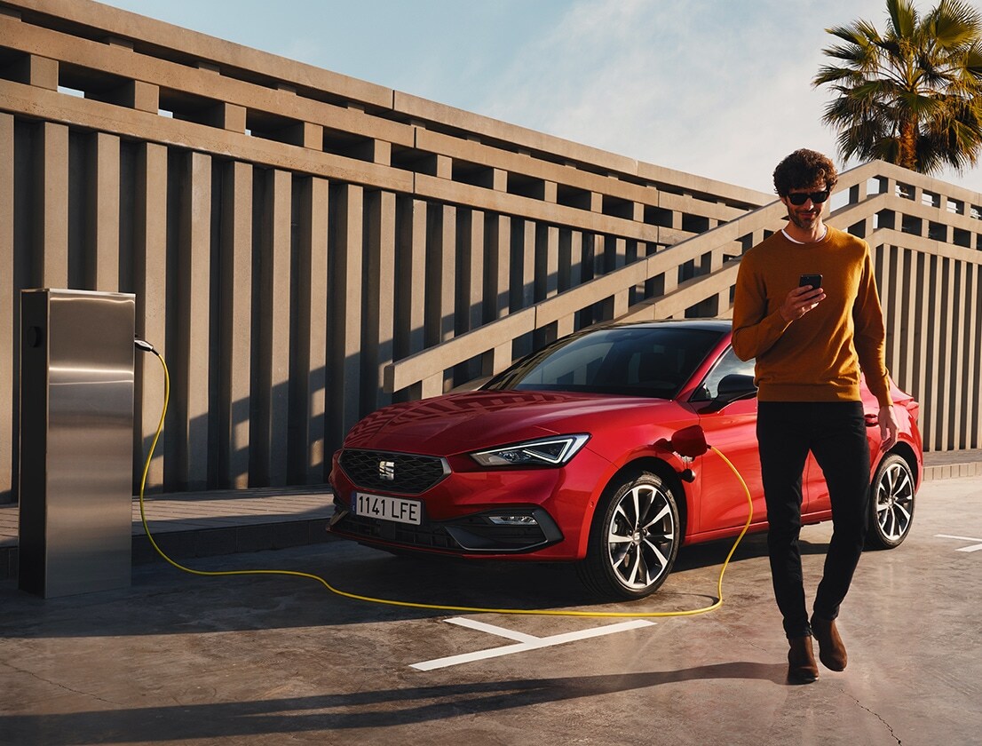 man walking away from the seat leon e-hybrid desire red colour using his smartphone