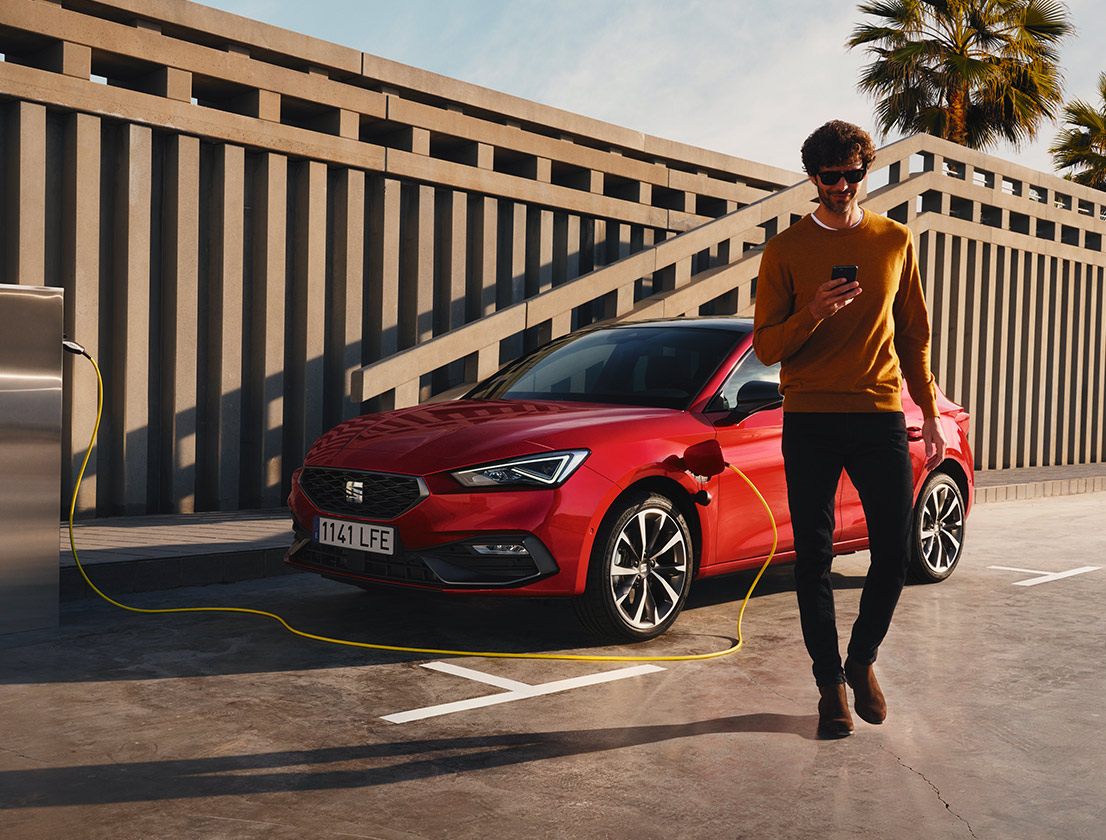 man walking away from the seat leon e-hybrid desire red colour using his smartphone