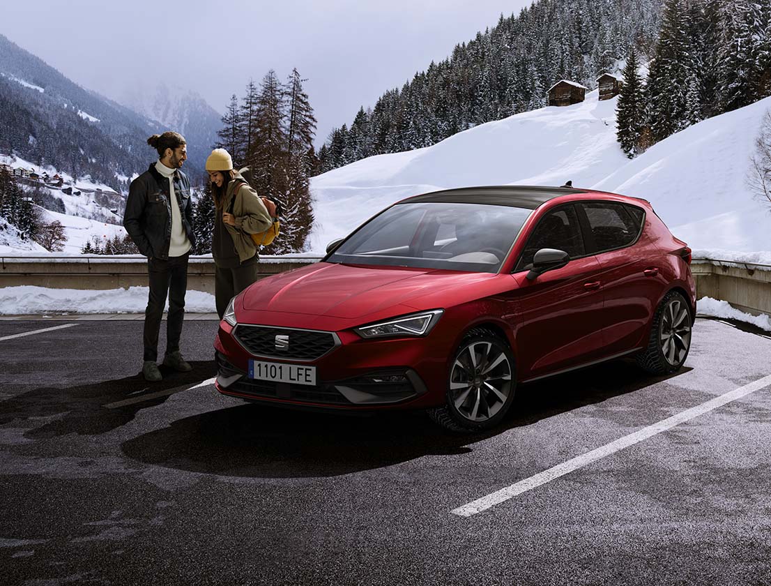 couple talking next to a SEAT Leon desire red colour in a snowy mountain