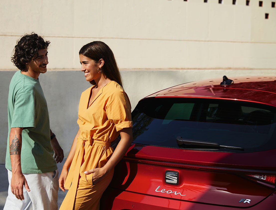 couple talking next to a SEAT Leon desire red colour