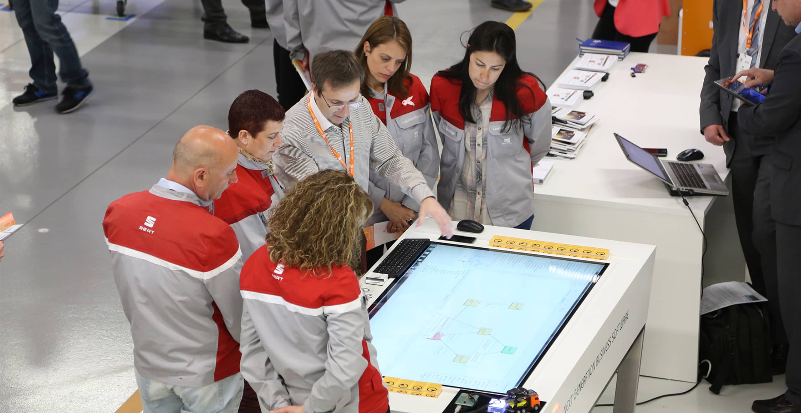 Team of workers gathered around an electronic display unit – SEAT Human Resources