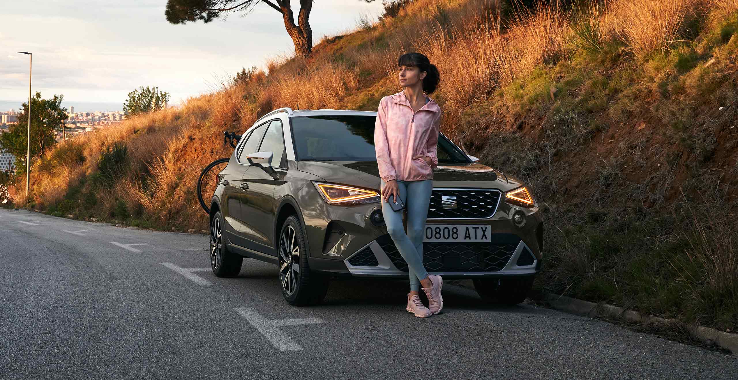 Woman leaning on front grille SEAT Arona dark camouflage colour with white roof