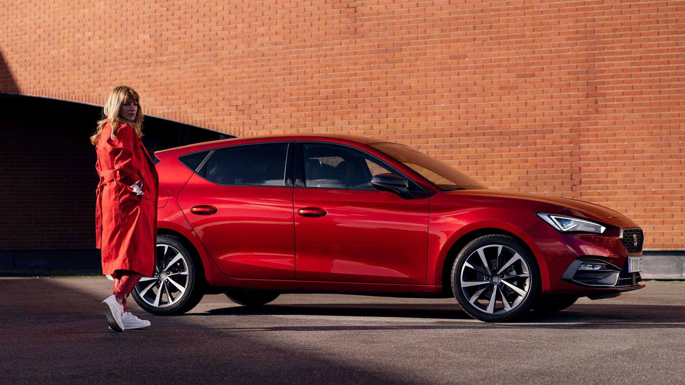 Woman in a red coat standing next to SEAT Leon 5d desire red colour