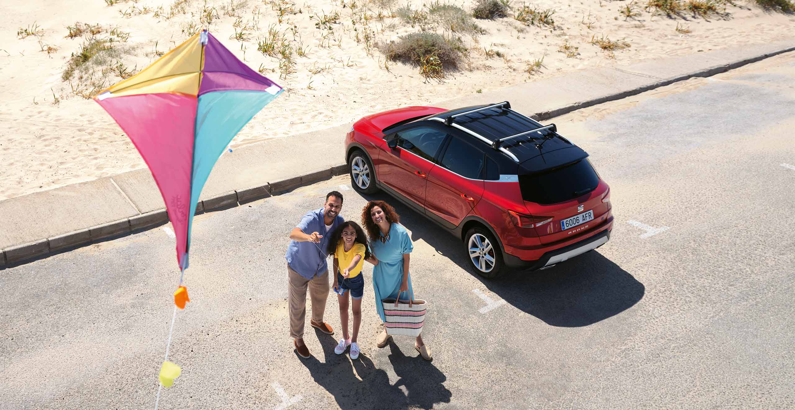 Family flying a kite next to their red SEAT Arona car