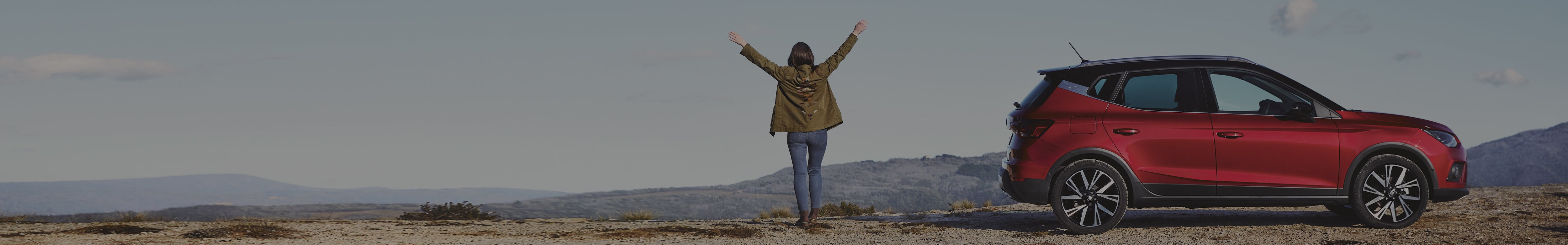 Woman on hill of the mountain next to a SEAT Arona in red colour 2